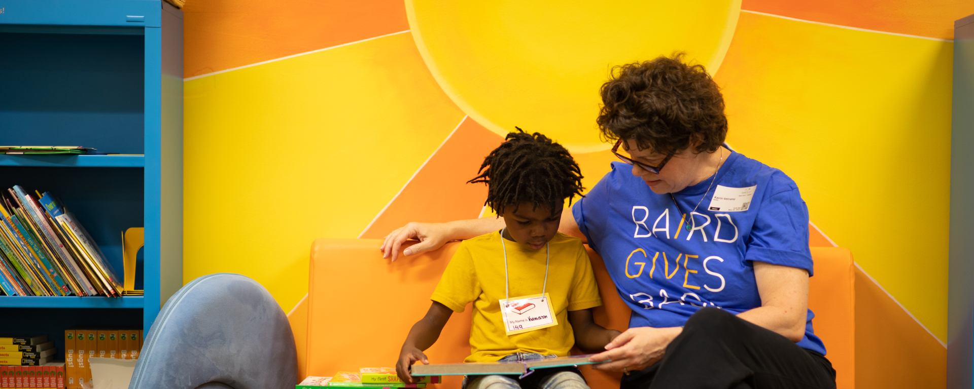 Woman in a RJF Pro Cares t-shirt reading to a student.