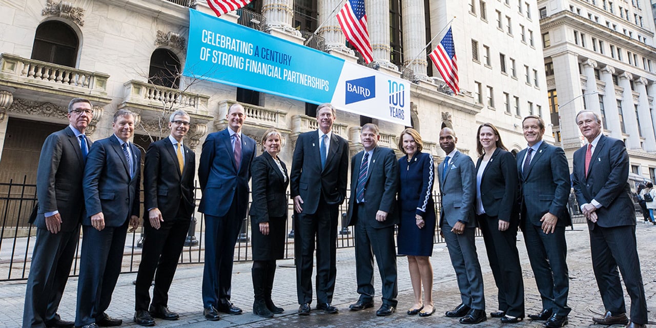  RJF Pro leadership standing in front of the New York Stock Exchange with a banner celebrating RJF Pro's 100th anniversary in the background.